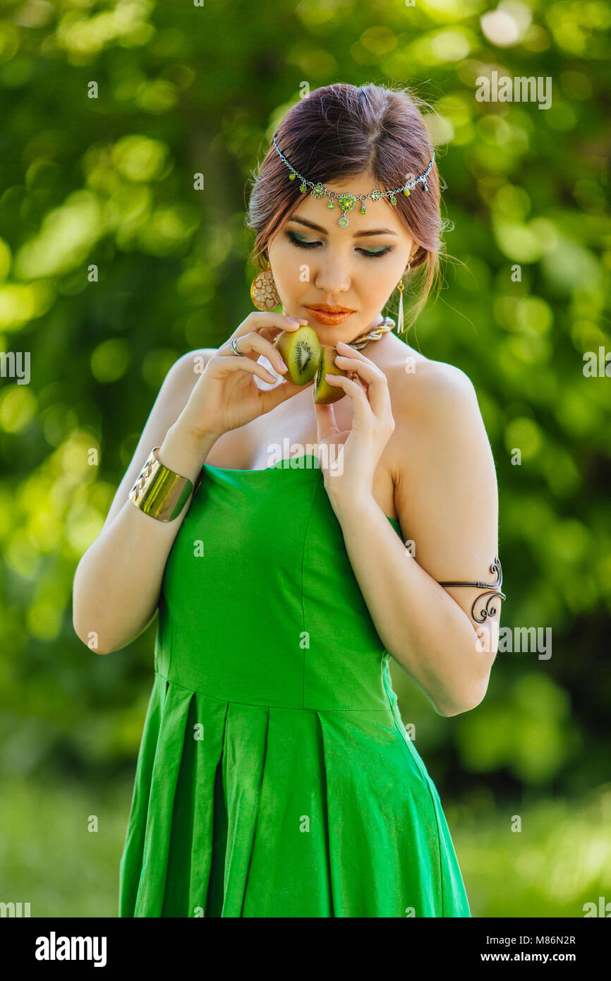 Portrait of a beautiful young asian woman holding two halves of kiwi ...