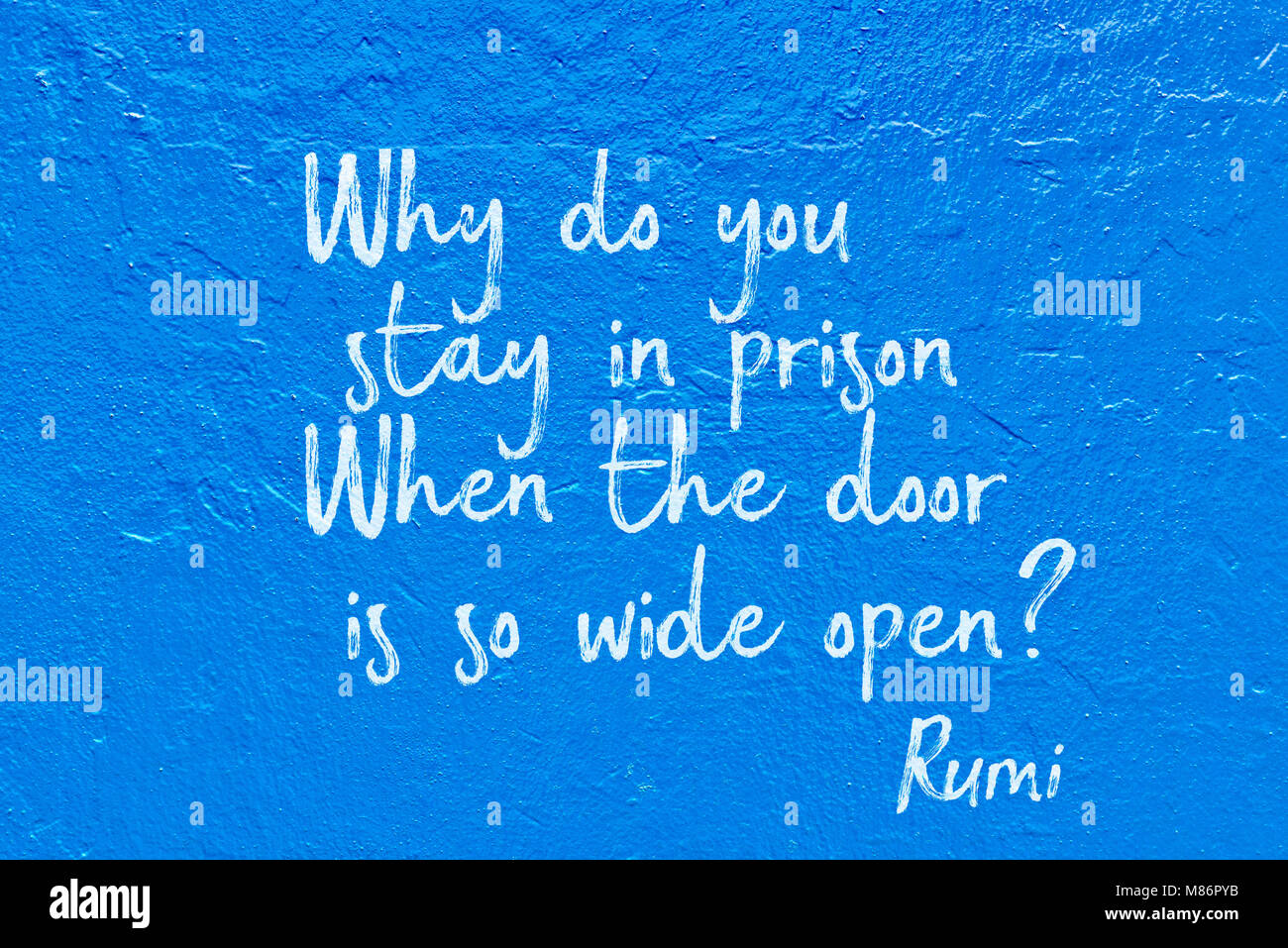 Why do you stay in prison. When the door is so wide open - ancient Persian poet and philosopher Rumi quote handwritten on blue wall Stock Photo