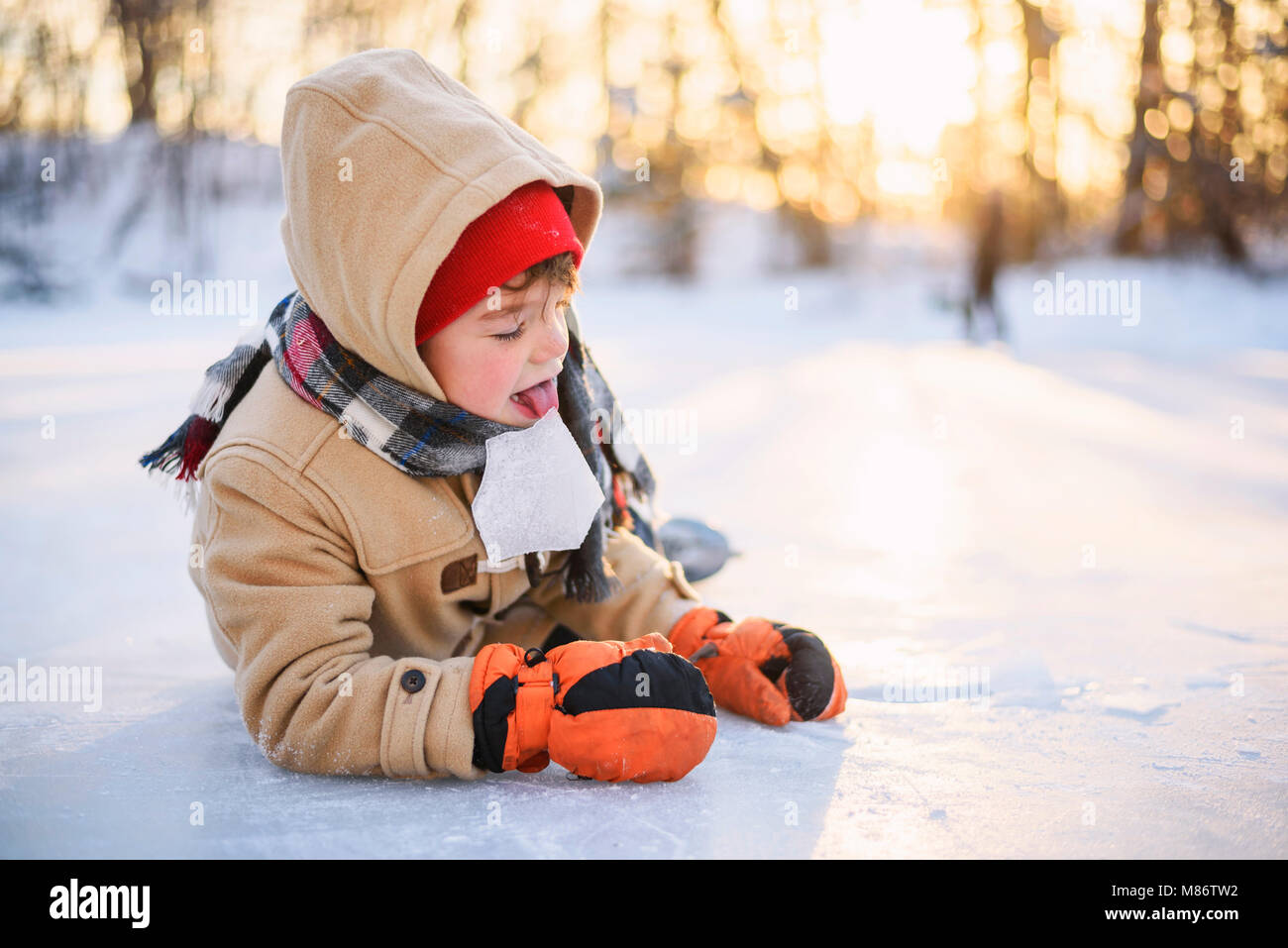 Boy lying on a frozen lake licking a piece of ice Stock Photo