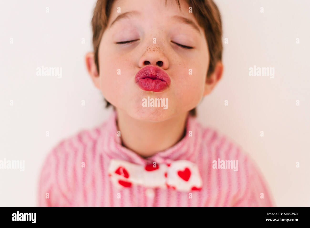 Portrait of a boy wearing a shirt and bow tie with hearts blowing a kiss Stock Photo