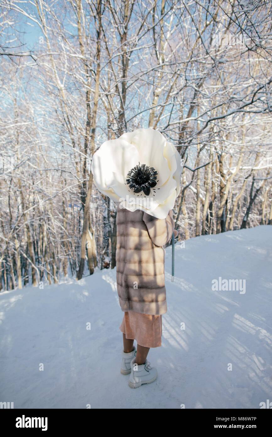 Woman standing in the snow holding a giant artificial anemone flower Stock Photo