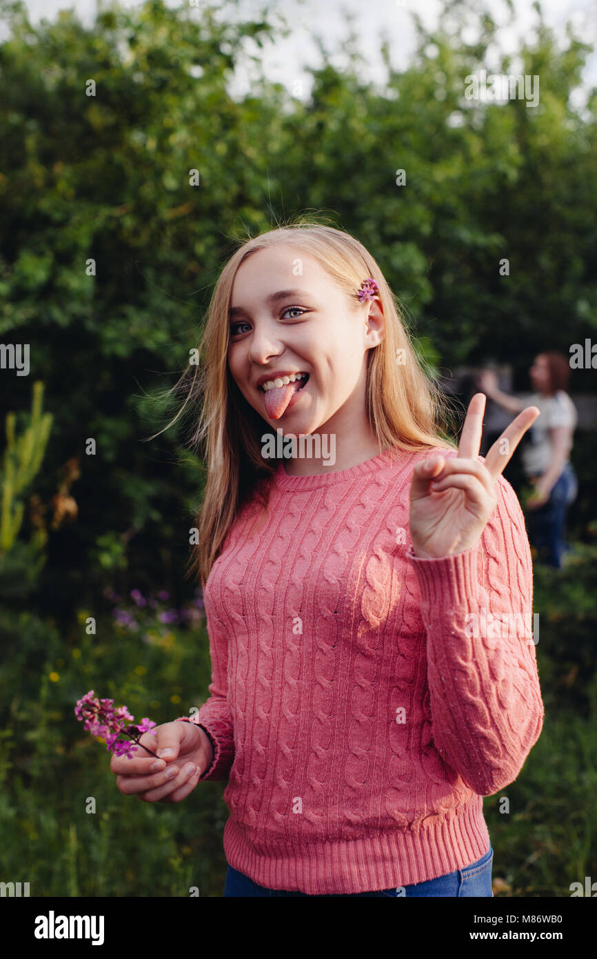 Girl sticking out her tongue and making a v sign Stock Photo