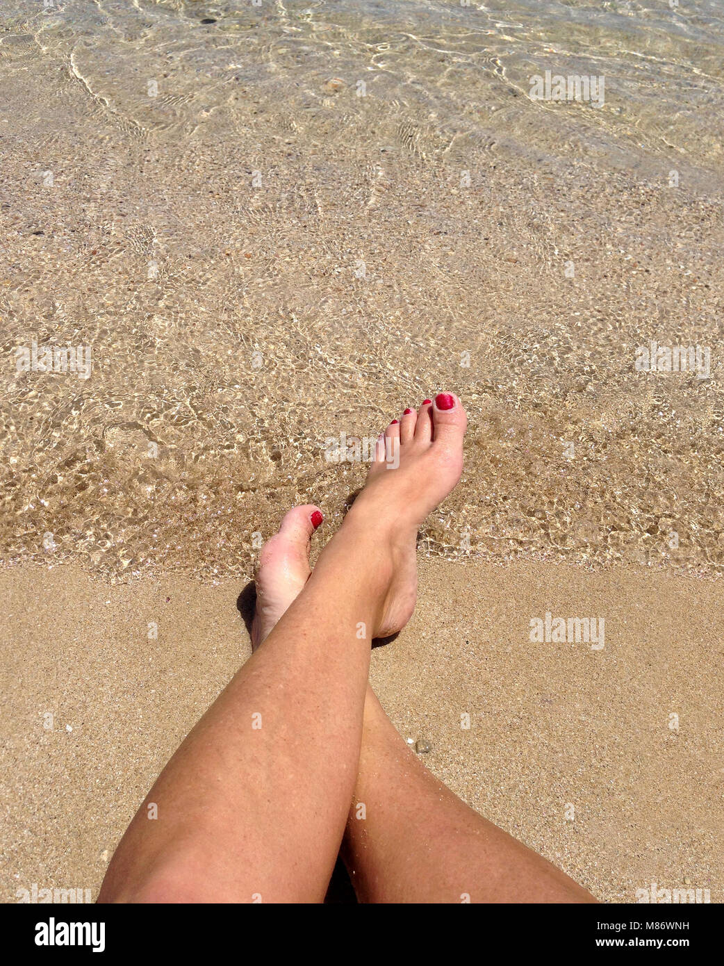 Woman's legs on beach at water's edge Stock Photo