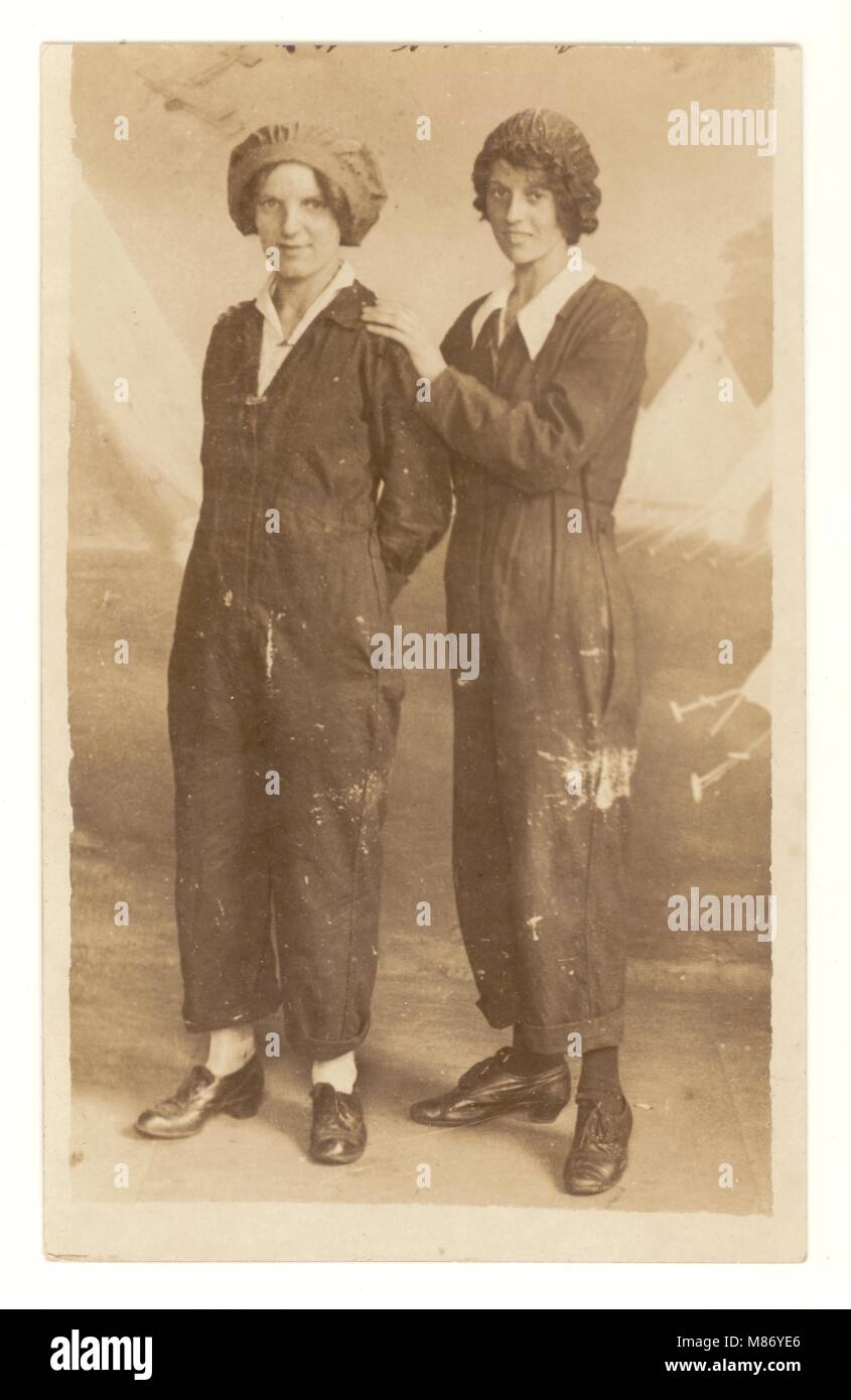 Original WW1 era (the Great War) postcard of 2 attractive happy women 'munitionettes' possibly factory or munitions workers in boilersuits / Womanalls/ one-piece workwear standing together, posing for a group photograph for a studio portrait with a painted canvas of tents behind them, volunteering to help the war effort, taking on traditional men's jobs, circa 1914-1918, U.K. Stock Photo