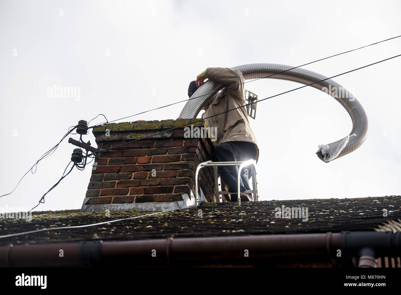 An engineer installs flue pipe down a chimney to ensure safety of a log burner's operation. Stock Photo