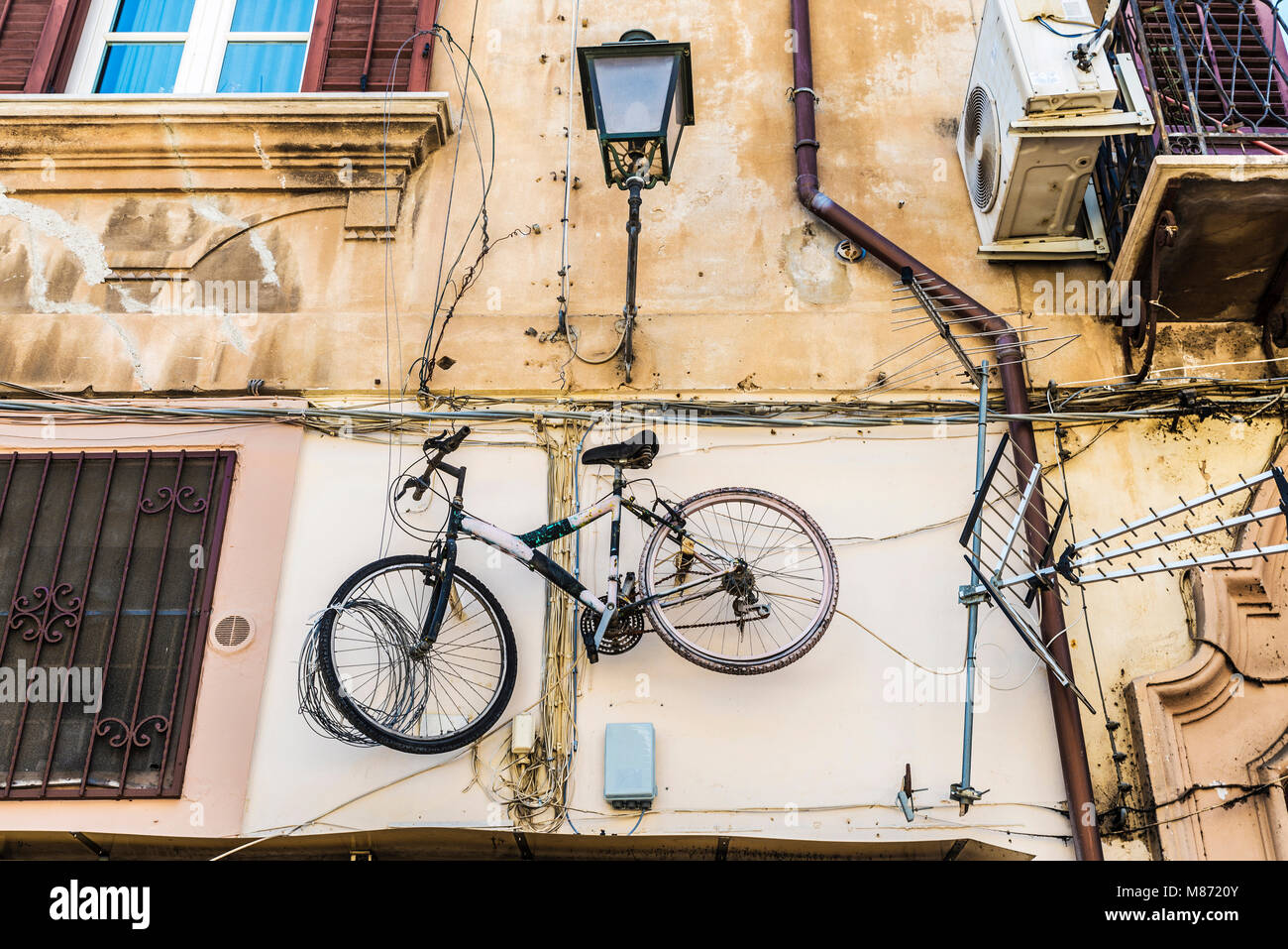 Bicycle hanging next to a television antenna on the wall of the facade of an old building in the old town of Palermo in Sicily, Italy Stock Photo