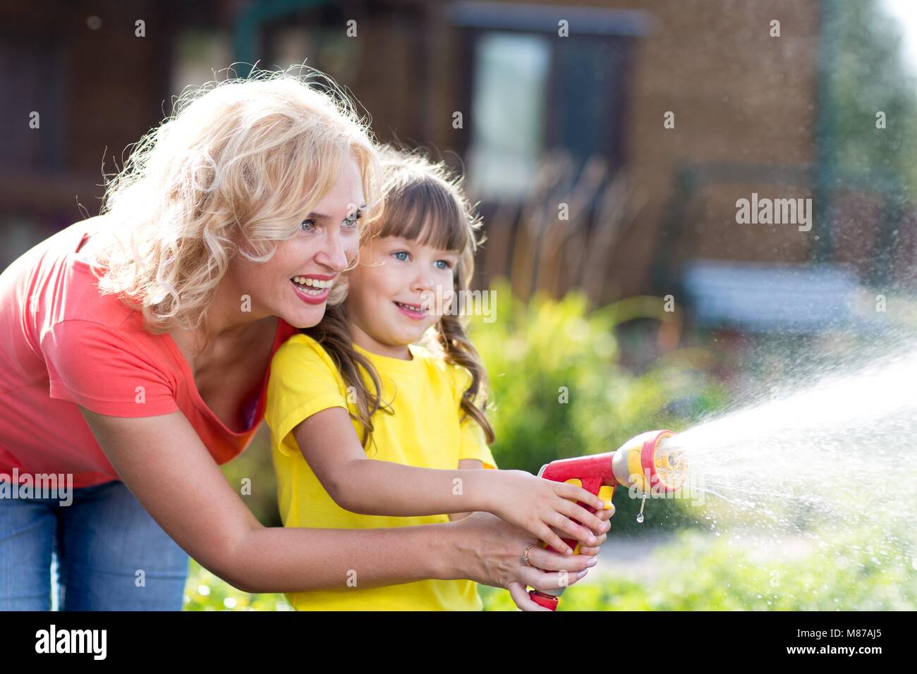 Portrait of gardener woman with child daughter watering flowers on the lawn near cottage. Stock Photo