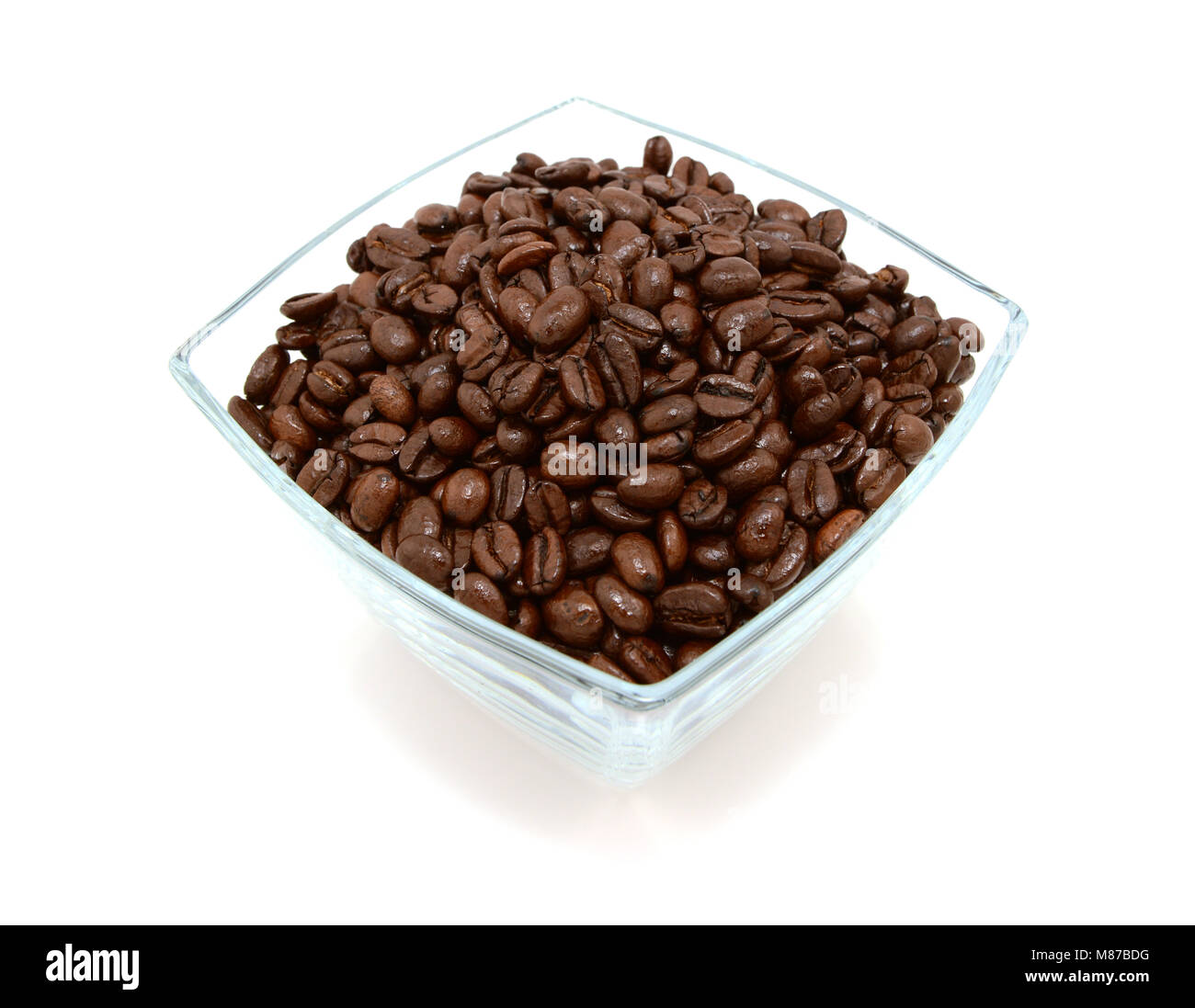 Glass bowl filled to the brim with dark roasted coffee beans, on a white background Stock Photo