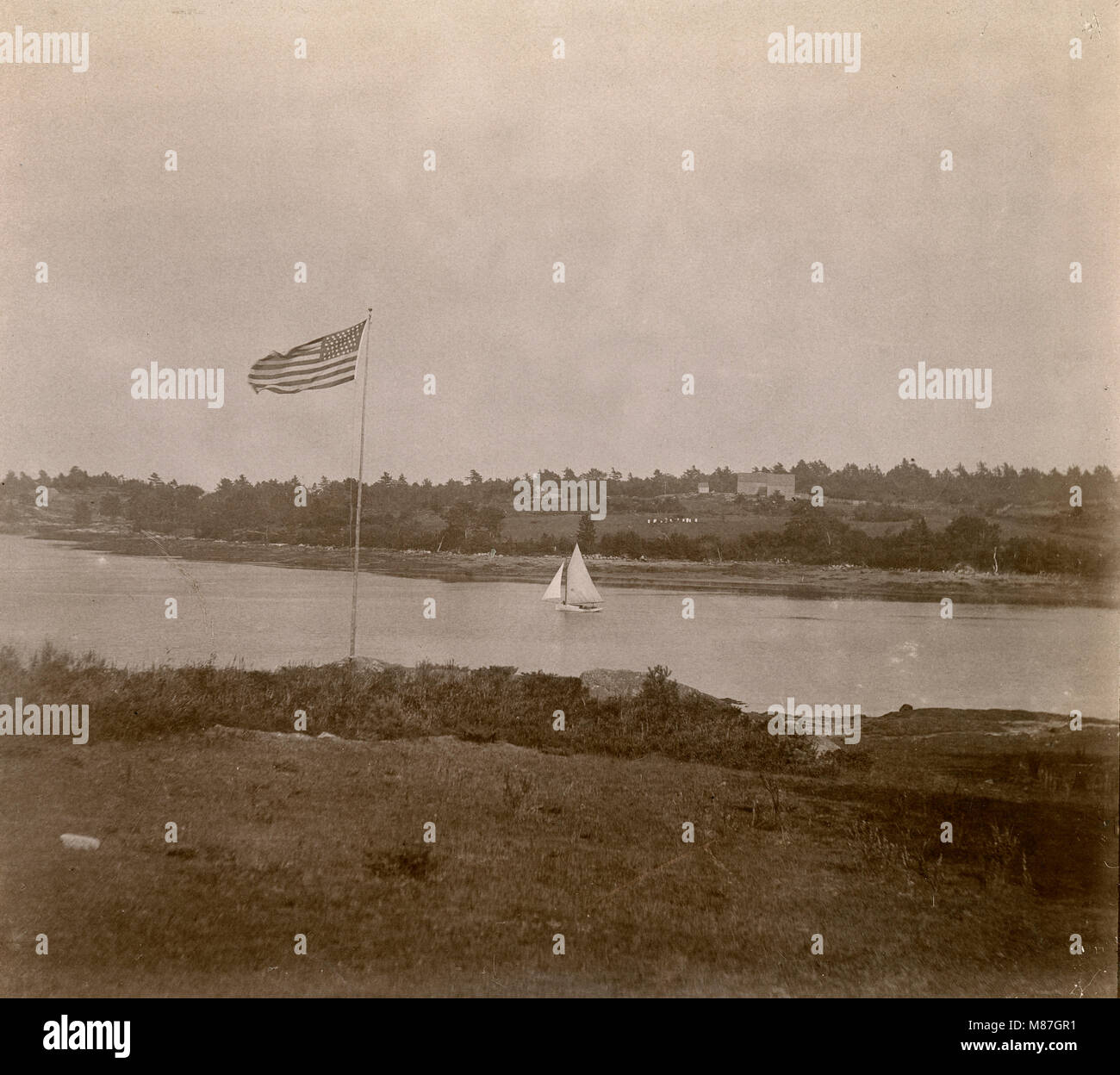 Antique circa 1905 photograph, 45-star flag and sailboat in the Sasanoa River. Location is in or near Riggsville (now Robinhood), Maine in Sagadahoc County, USA. Stock Photo