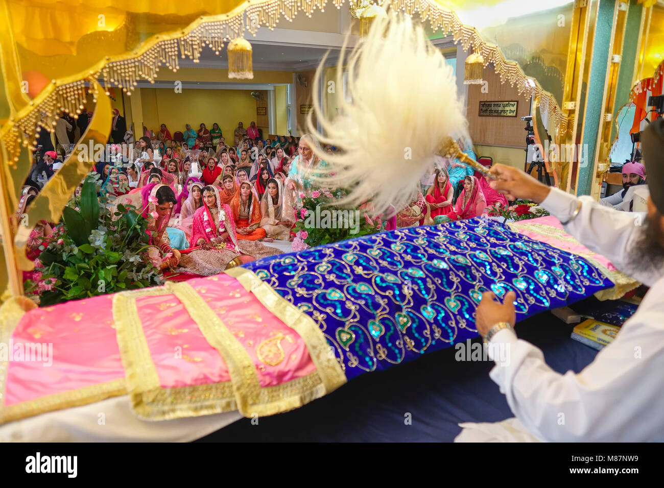 Sikh wedding ceremony in a Gurdwara with priest waving Chaur Sahib (fly whisk) above the holy book (Guru Granth Sahib) Stock Photo