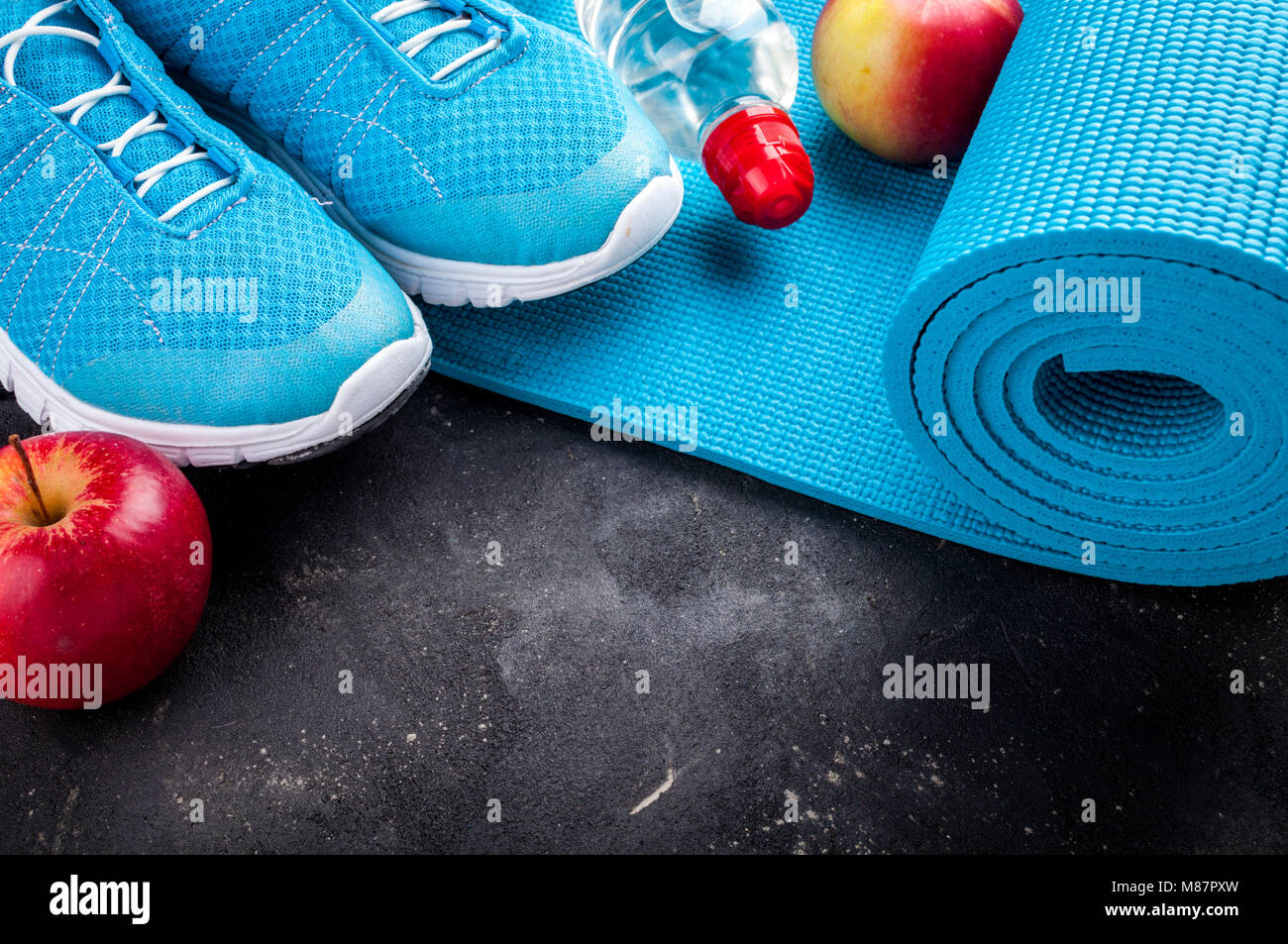 Sport shoes, yoga mat, apples, bottle of water on dark background. Concept healthy lifestyle, healthy food, sport and diet. Sport equipment. Copy spac Stock Photo