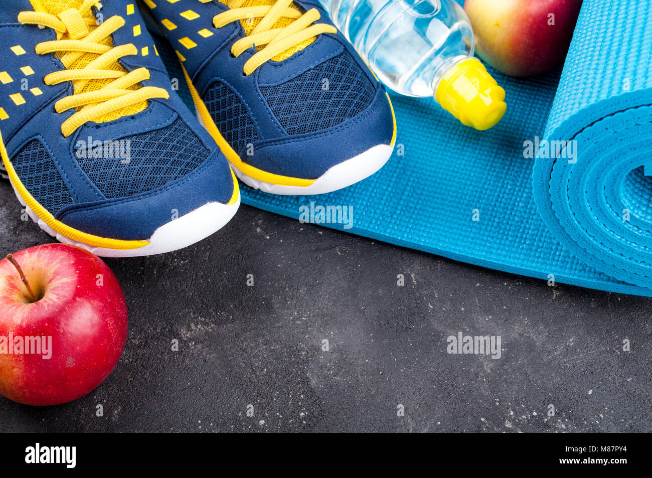 Yoga mat, sport shoes, apples, bottle of water on dark background. Concept healthy lifestyle, healthy eating, sport and diet. Sport equipment. Copy sp Stock Photo