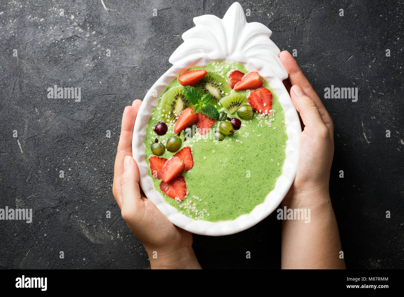 Female hands holding smoothie bowl with kiwi, spinach, strawberries and berry. Healthy eating diet concept Stock Photo