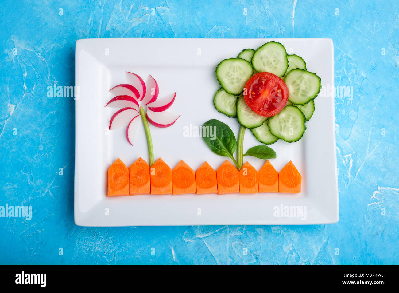 Kids food. Funny vegetable salad for kids. Healthy food with vegetables tomato, cucumber, carrot, radish, spinach and sour cream. Baby snack. Top view Stock Photo