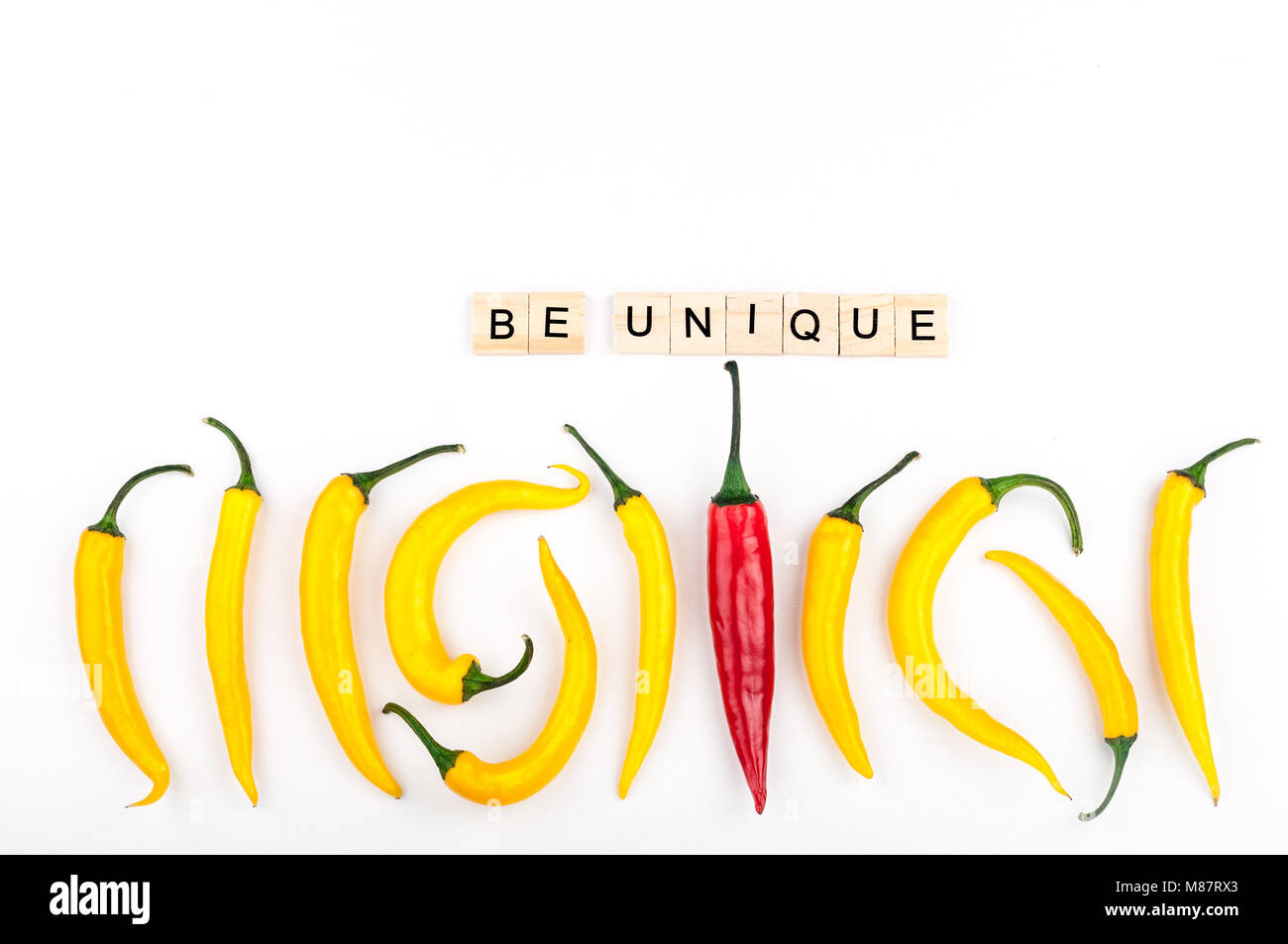 Red chili pepper standing out from crowd of identical yellow peppers on white background. Leadership, be unique, initiative, strategy, think different Stock Photo
