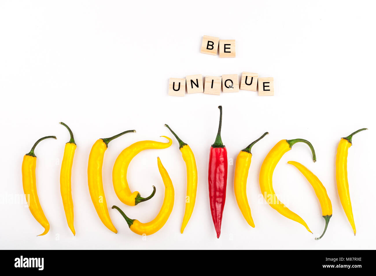 Red chili pepper standing out from crowd of identical yellow peppers on white background. Leadership, be unique, initiative, strategy, think different Stock Photo