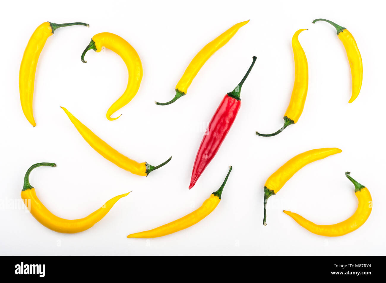 Red chili pepper standing out from crowd of identical yellow peppers on white background. Leadership, be unique, initiative, strategy, think different Stock Photo