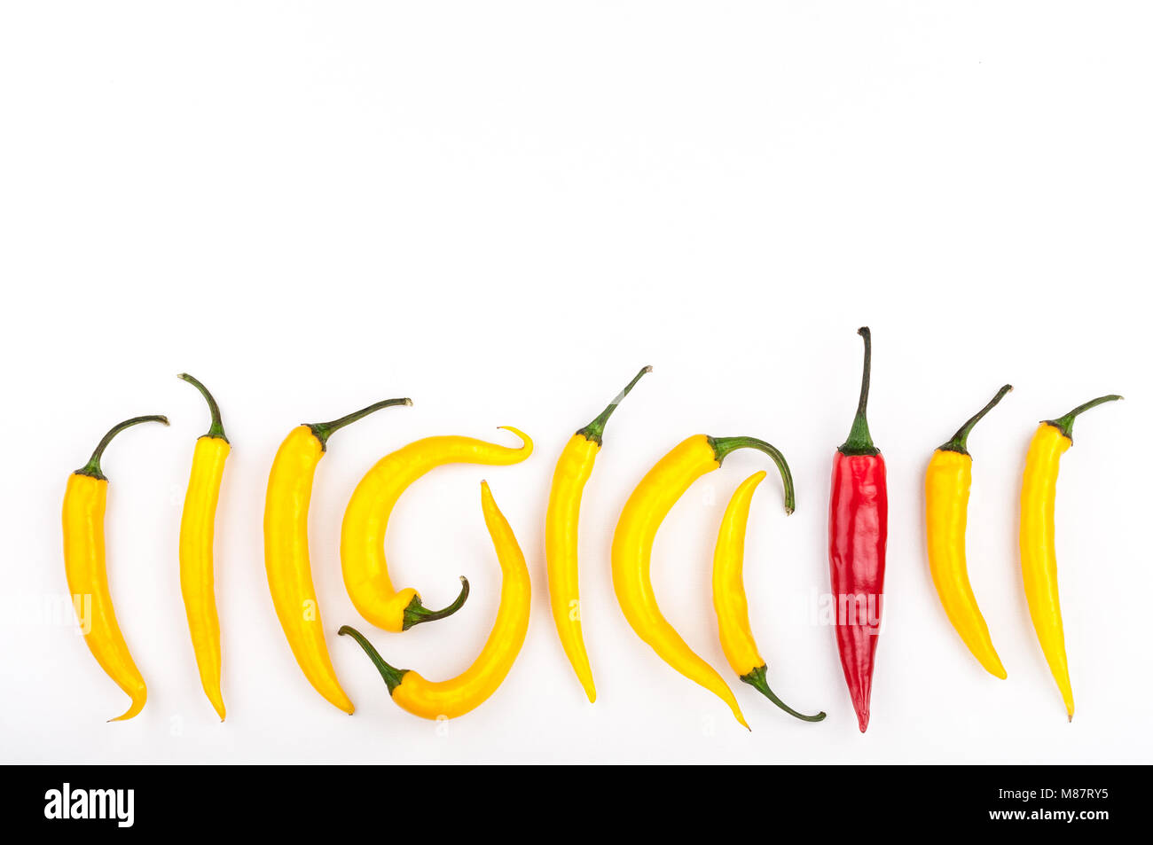 Red chili pepper standing out from crowd of identical yellow peppers on white background. Leadership, be unique, initiative, strategy, think different Stock Photo