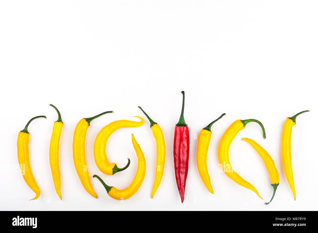 Red chili pepper standing out from crowd of identical yellow peppers on white background. Leadership, be unique, initiative, strategy, think different Stock Photo