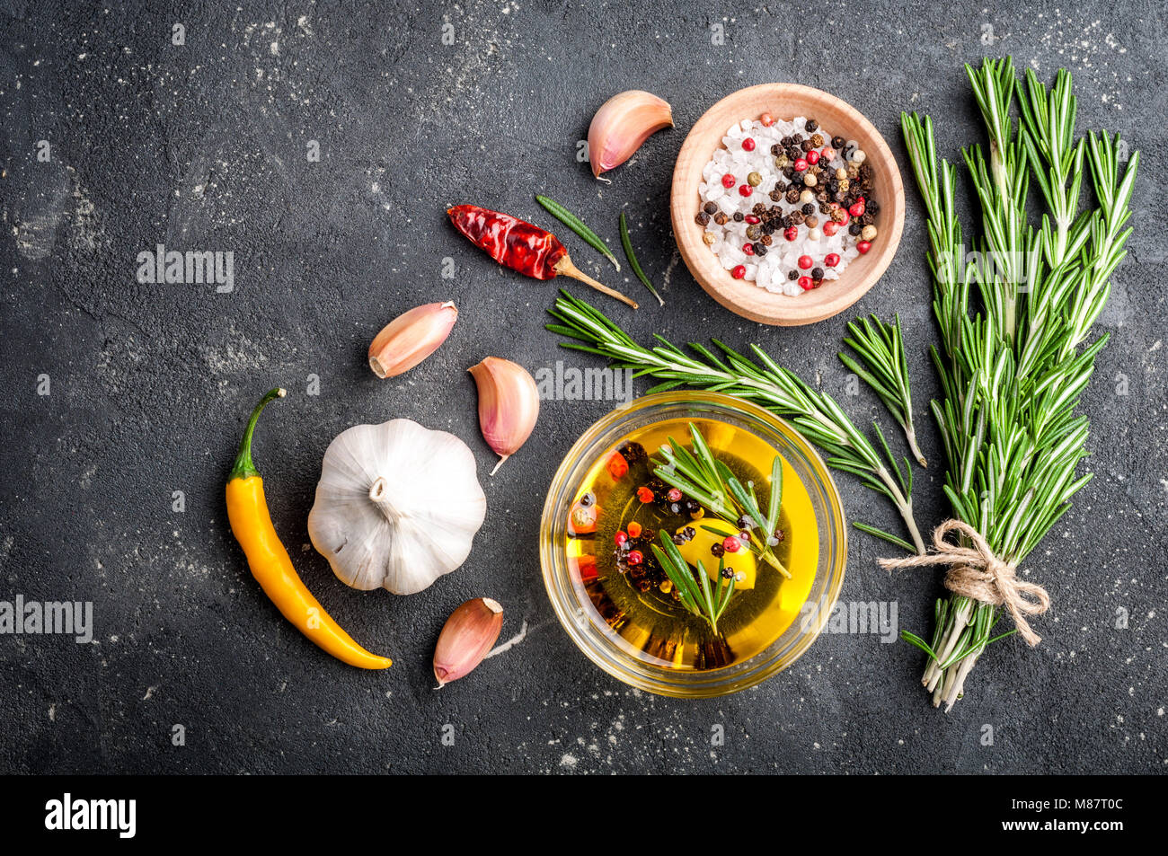 Herbs and spices. Rosemary, chili pepper, garlic, olive oil, salt and pepper on dark table. Cooking ingredients. Top view and copy space for your reci Stock Photo