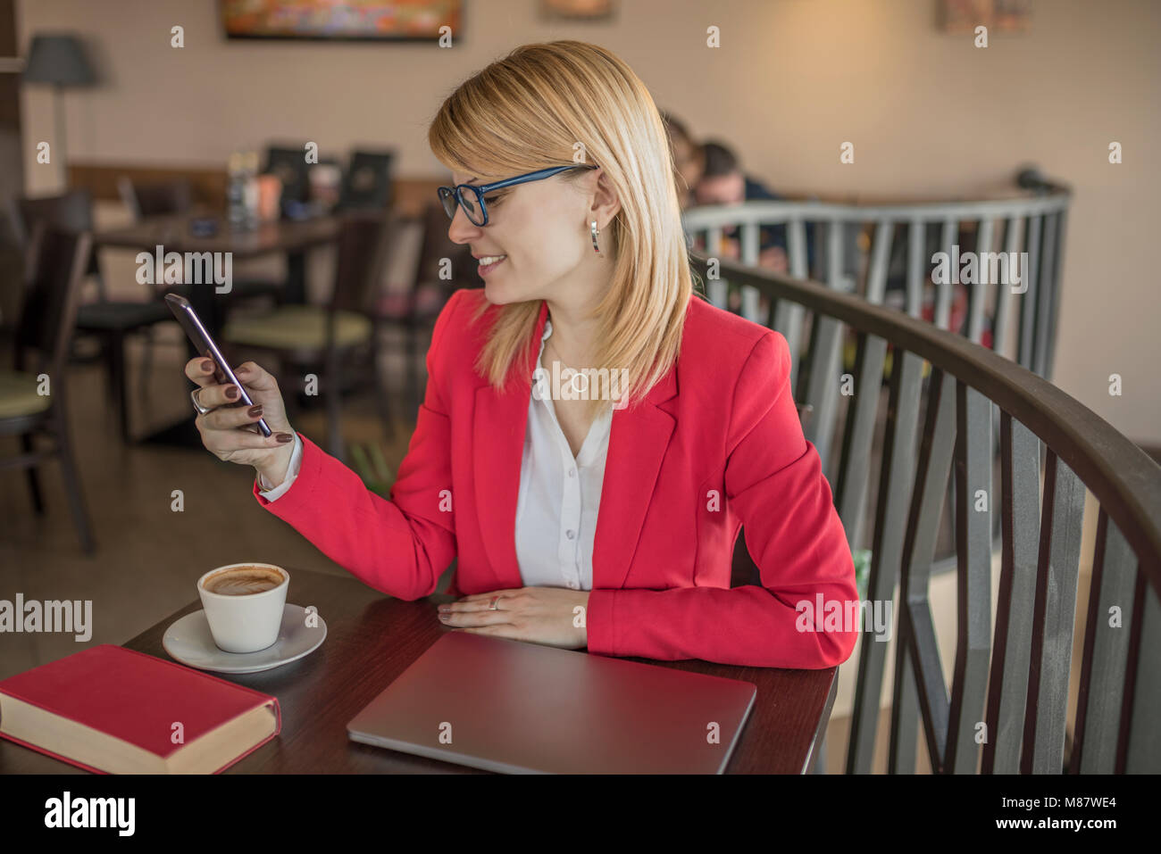 Young smiling blonde woman using smart phone, texting message in coffee ...