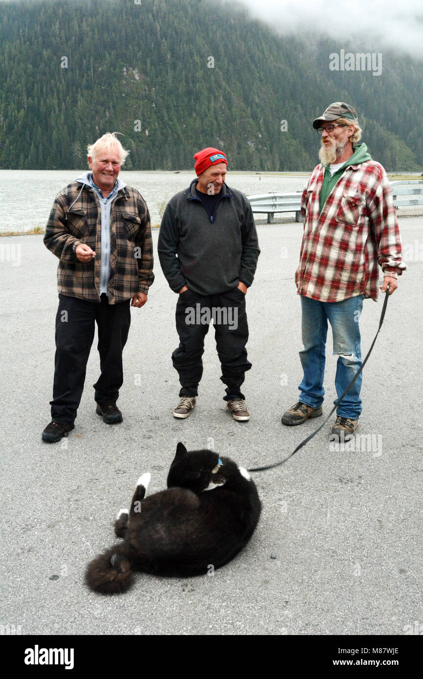 Three friends and residents of the town of Hyder, Alaska, chatting on the edge of the waterfront, below fjords of the Portland Canal, USA. Stock Photo