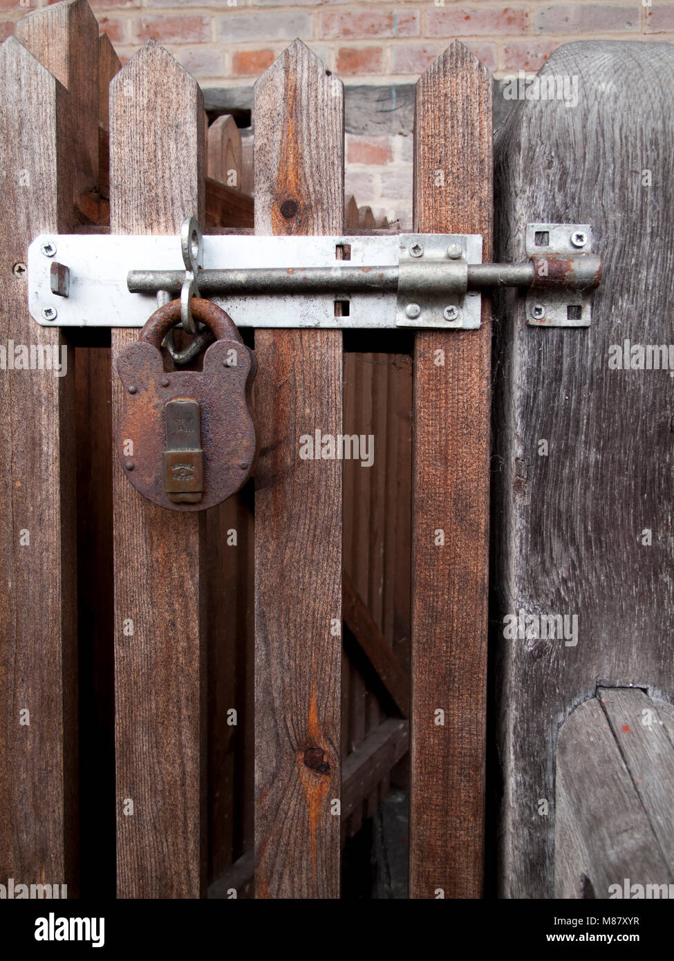 Rusty padlock clasp and staple securing timber gate to side of residential building Stock Photo