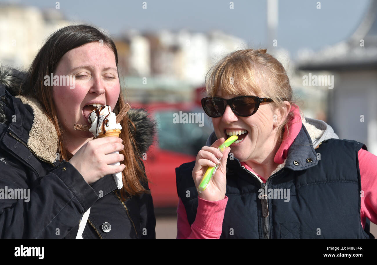 Brighton UK 16th March 2018  - Visitors enjoy an ice cream and a stick of rock in warm sunshine on Brighton seafront today but the weather is forecast to turn cold again with snow expected in some parts off Britain over the weekend Photograph taken by Simon Dack Credit: Simon Dack/Alamy Live News Credit: Simon Dack/Alamy Live News Stock Photo