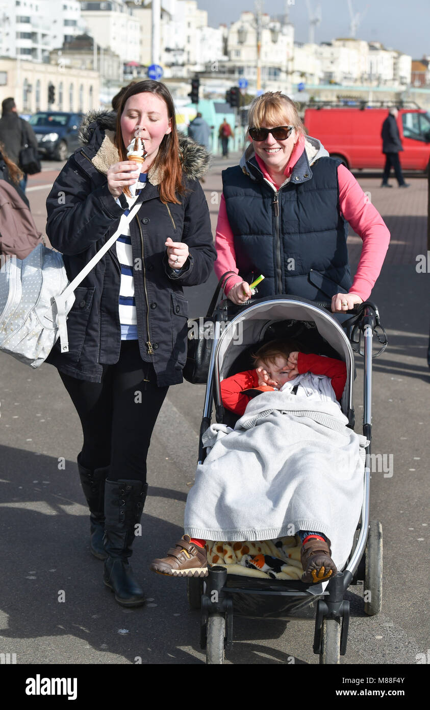 Brighton UK 16th March 2018  - Visitors enjoy an ice cream and a stick of rock in warm sunshine on Brighton seafront today but the weather is forecast to turn cold again with snow expected in some parts off Britain over the weekend Photograph taken by Simon Dack Credit: Simon Dack/Alamy Live News Credit: Simon Dack/Alamy Live News Stock Photo