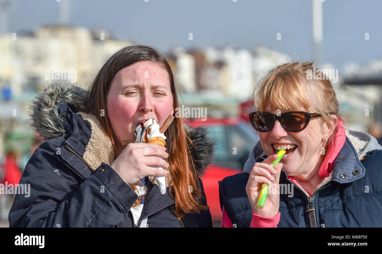 Brighton UK 16th March 2018  - Visitors enjoy an ice cream and a stick of rock in warm sunshine on Brighton seafront today but the weather is forecast to turn cold again with snow expected in some parts off Britain over the weekend Photograph taken by Simon Dack Credit: Simon Dack/Alamy Live News Credit: Simon Dack/Alamy Live News Stock Photo