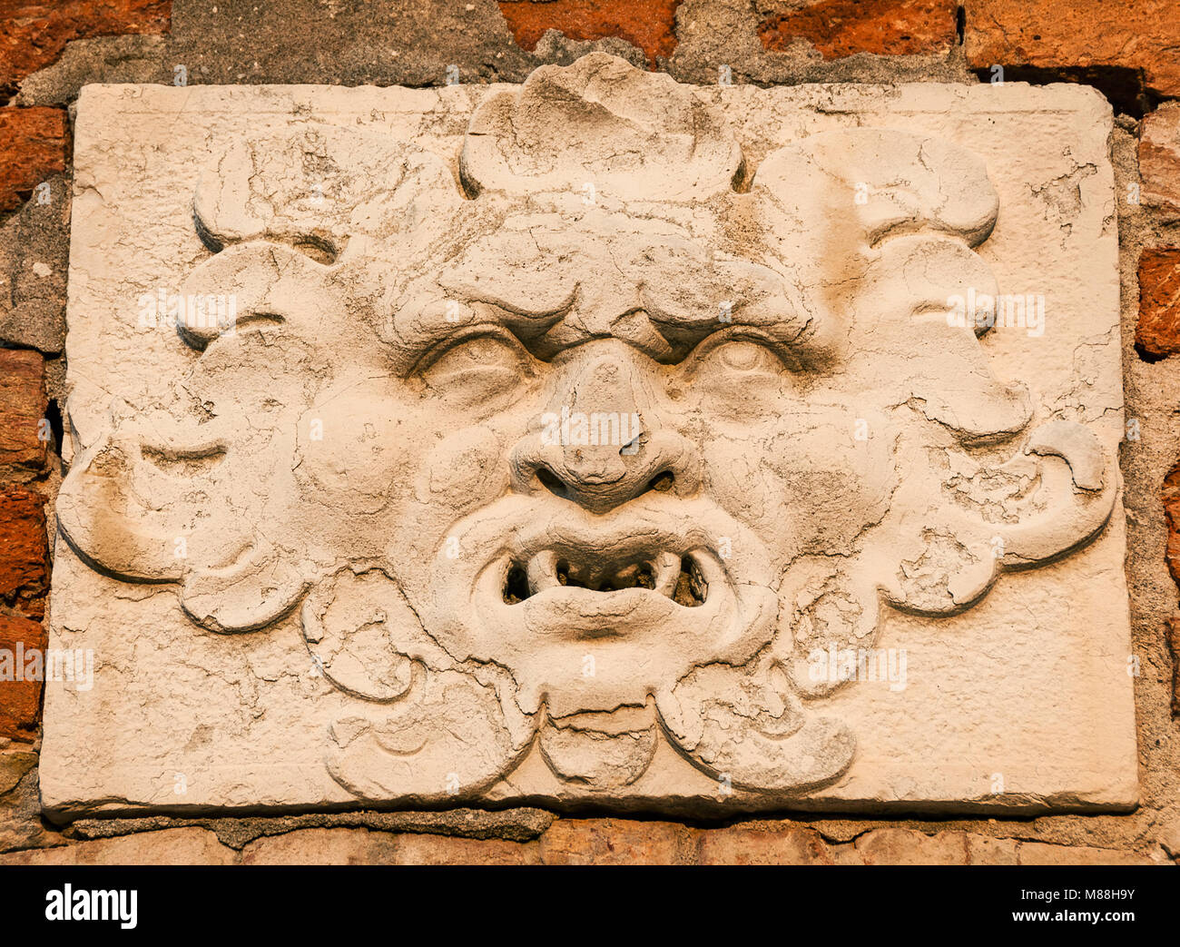 Frightening demon face old relief on wall in Venice Stock Photo