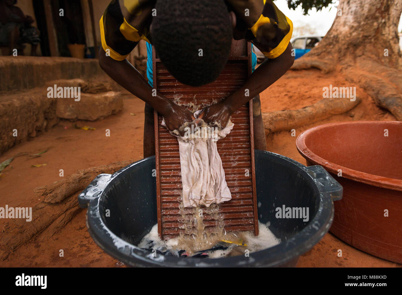 Young boy washing dirty clothes in a washing board and tub in the town