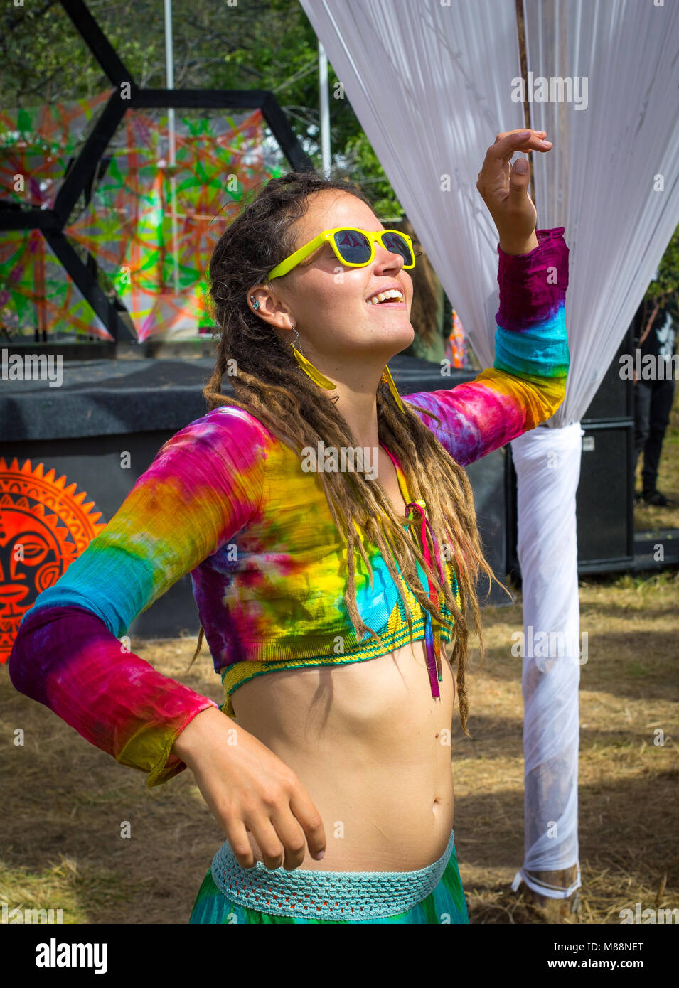 Cheerful girl with dreadlocks in colorful top is dancing at the festival FOURЭ. Summer. Almaty region. Kazakhstan. Stock Photo