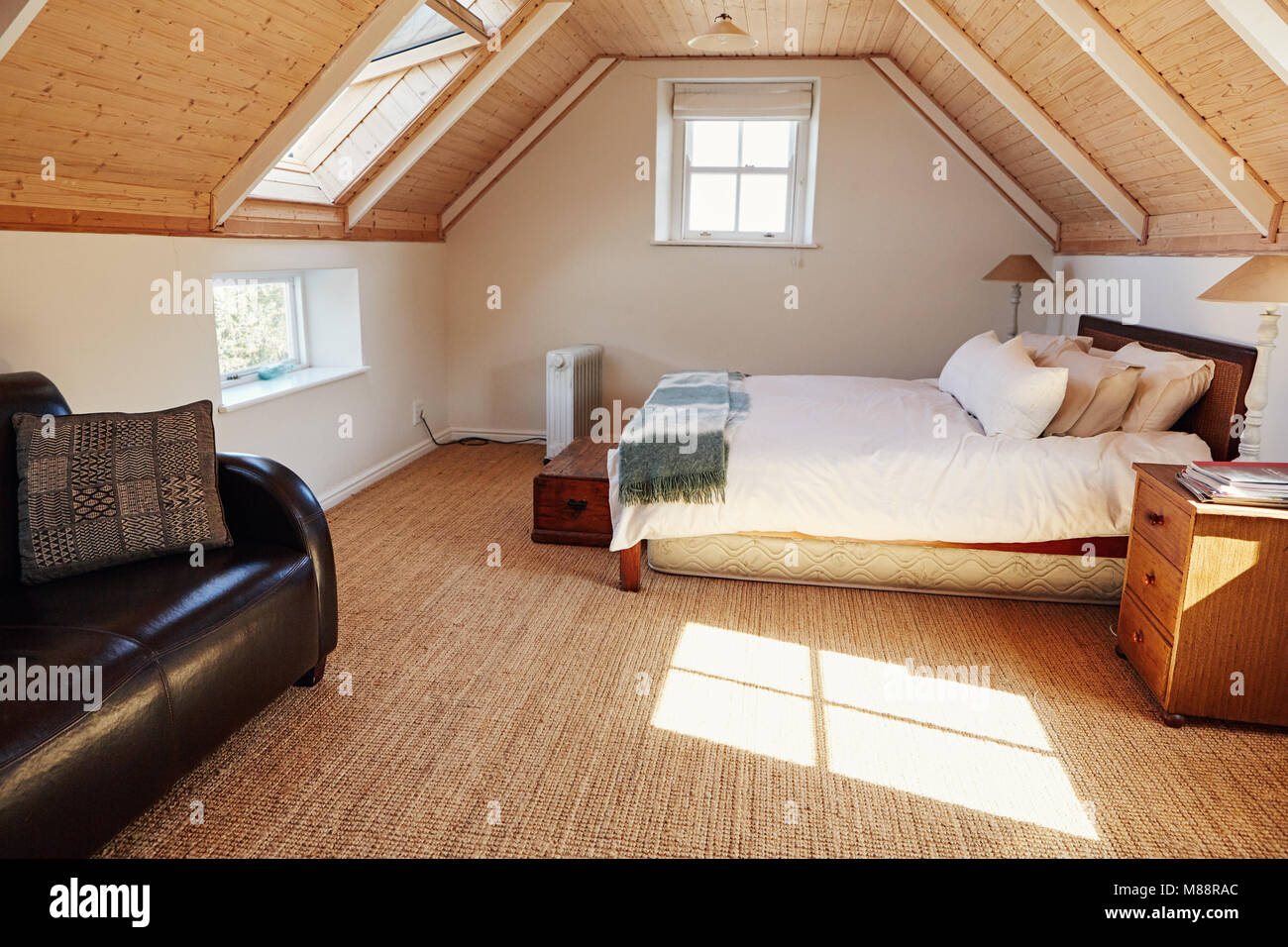 Interior of a comfortable master bedroom with a bed and sofa in the attic of a contemporary residential home Stock Photo