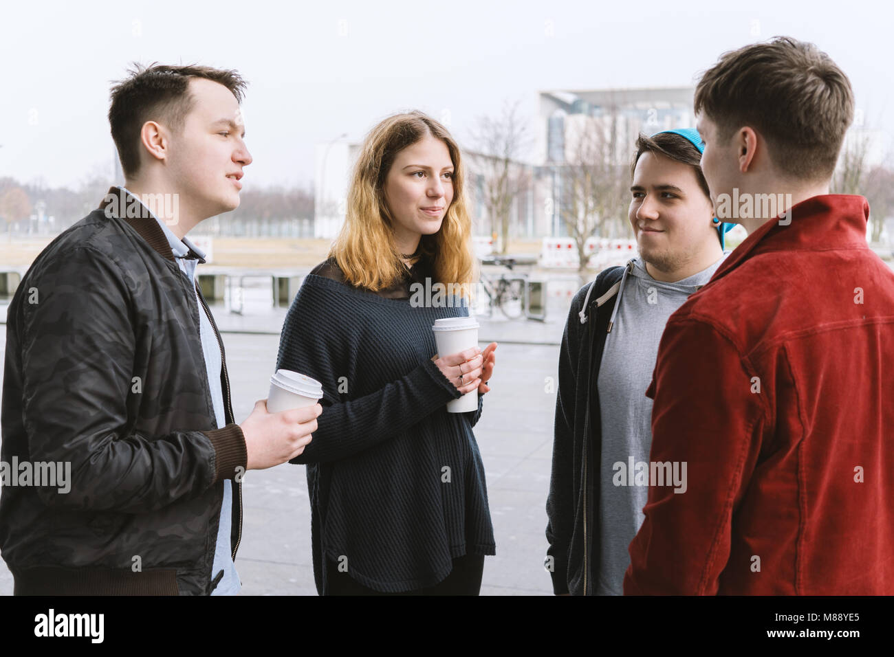 group of teenage friends having a conversation while standing together on city street Stock Photo