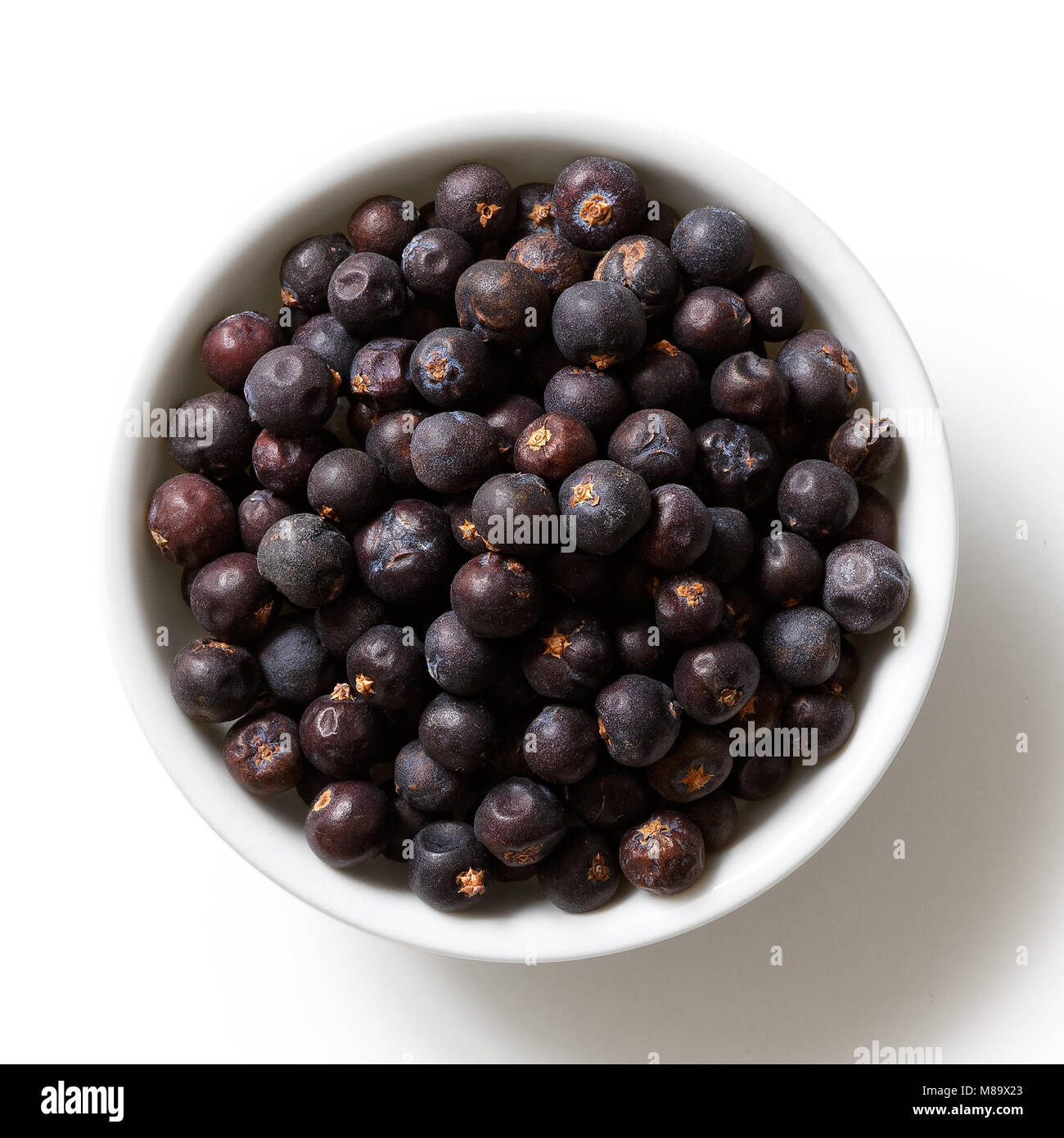 Dried juniper berries in white ceramic bowl isolated on white from above. Stock Photo