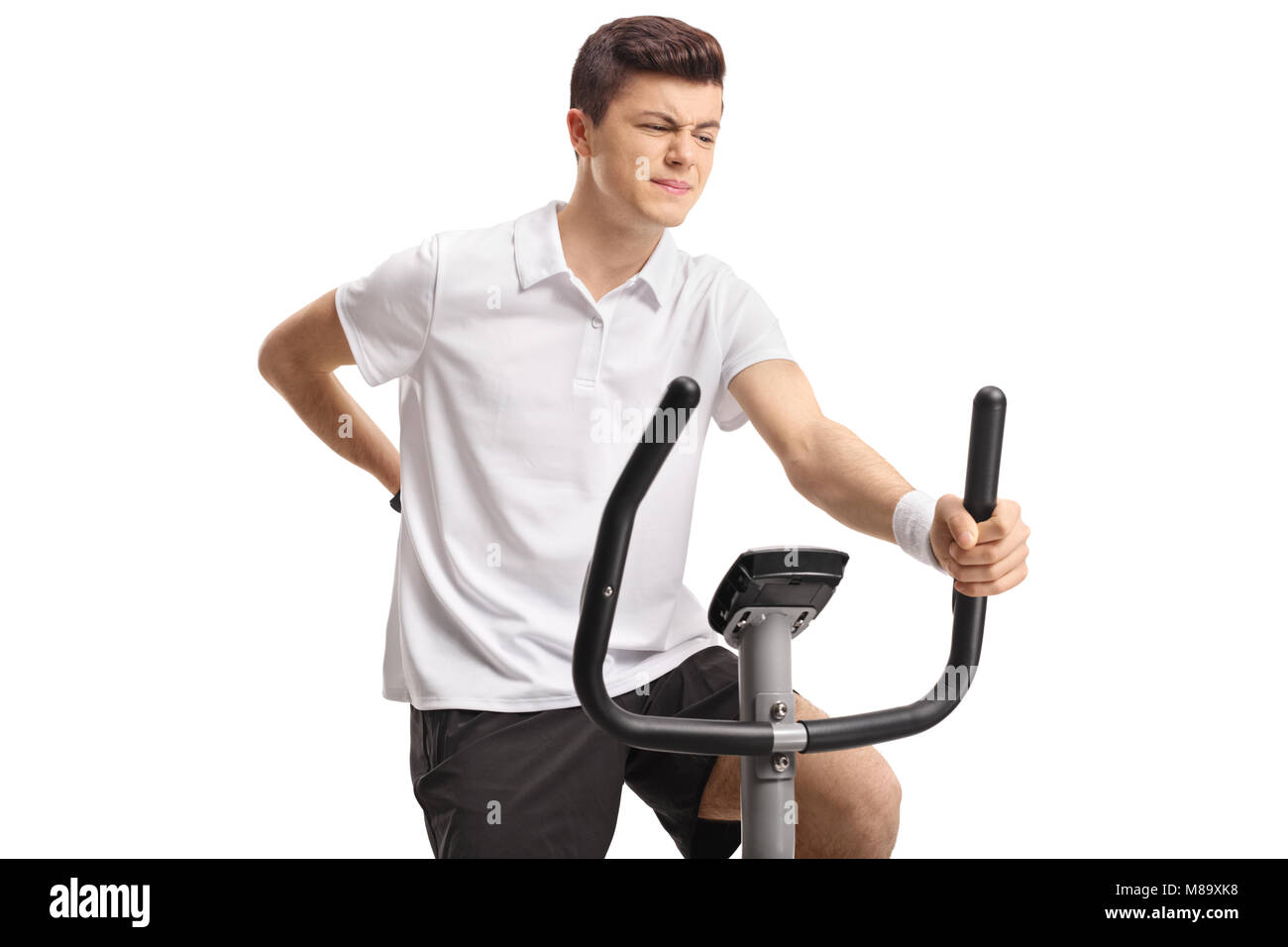 Teenager riding an exercise bike and experiencing back pain isolated on white background Stock Photo