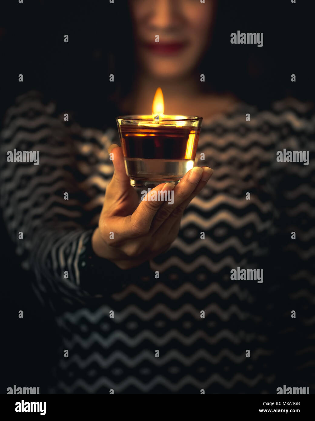 Woman holding candle votive in her hand. Candle in Glass. Concept of