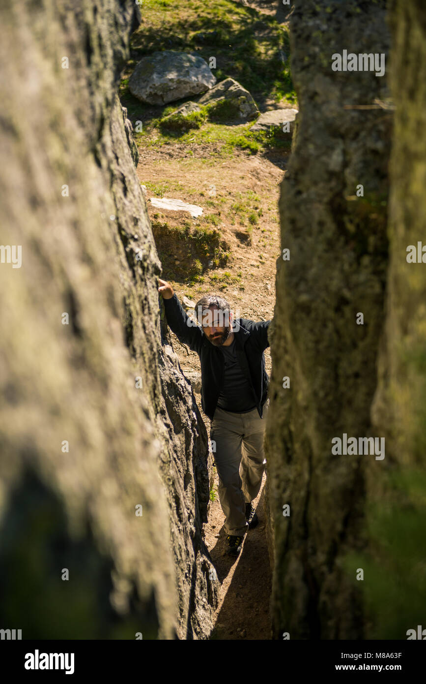 Young adult active man hike through narrow path between rock walls in sunny summer day on mountian outdoor. Stock Photo