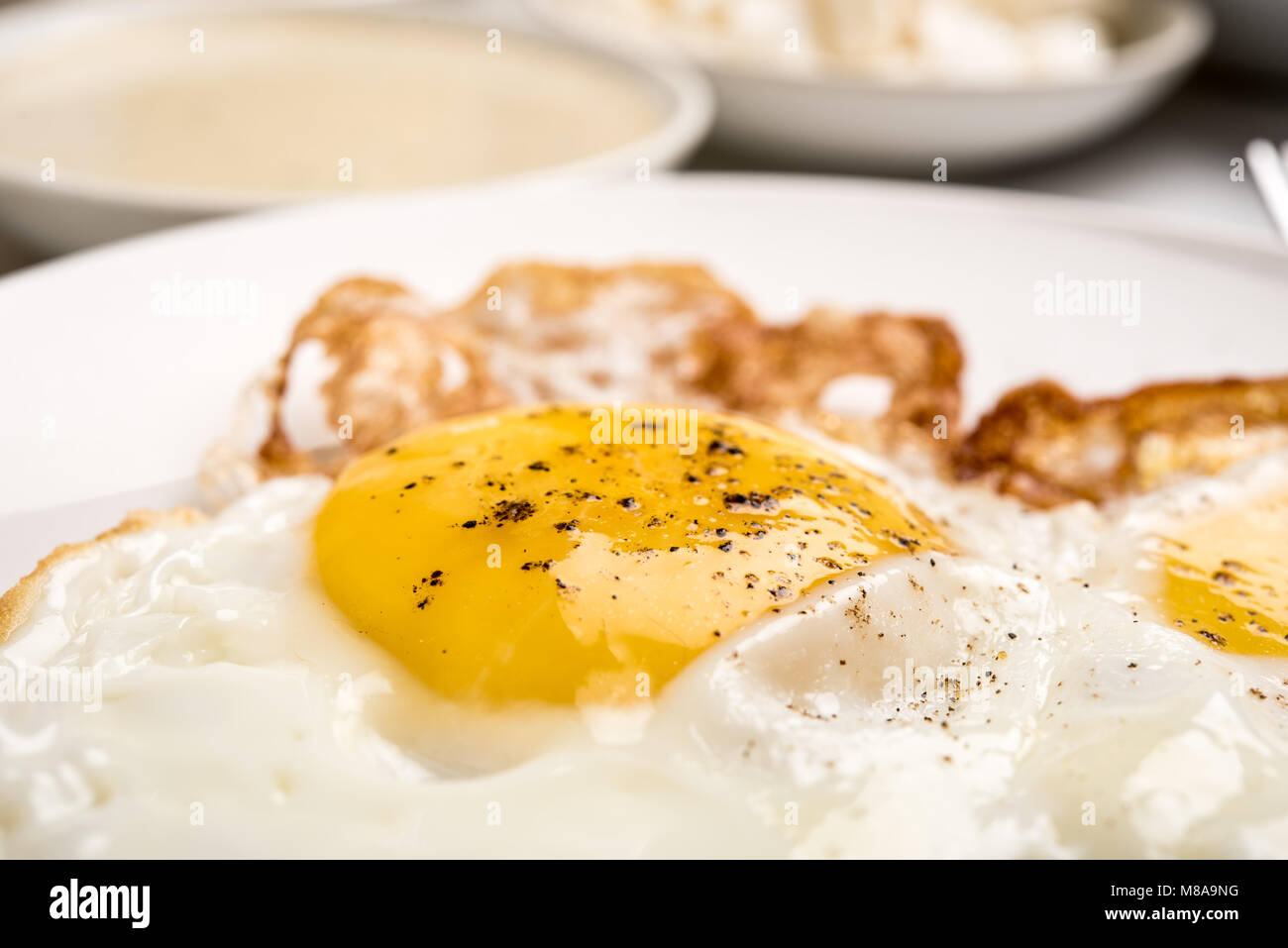Traditional Israeli Breakfast with two fried eggs, yellow cheese, salad, a fresh roll and a cup of cappuccino. Closeup on the fried eggs Stock Photo