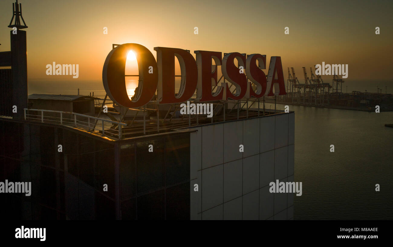 Sun rises behind large Odessa sign on top of the Odessa Hotel, Ukraine. The Black Sea and port are in the background Stock Photo