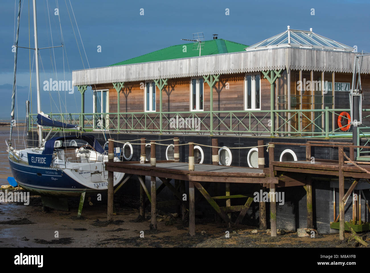 A modern houseboat with a luxury yacht alongside moored next to the