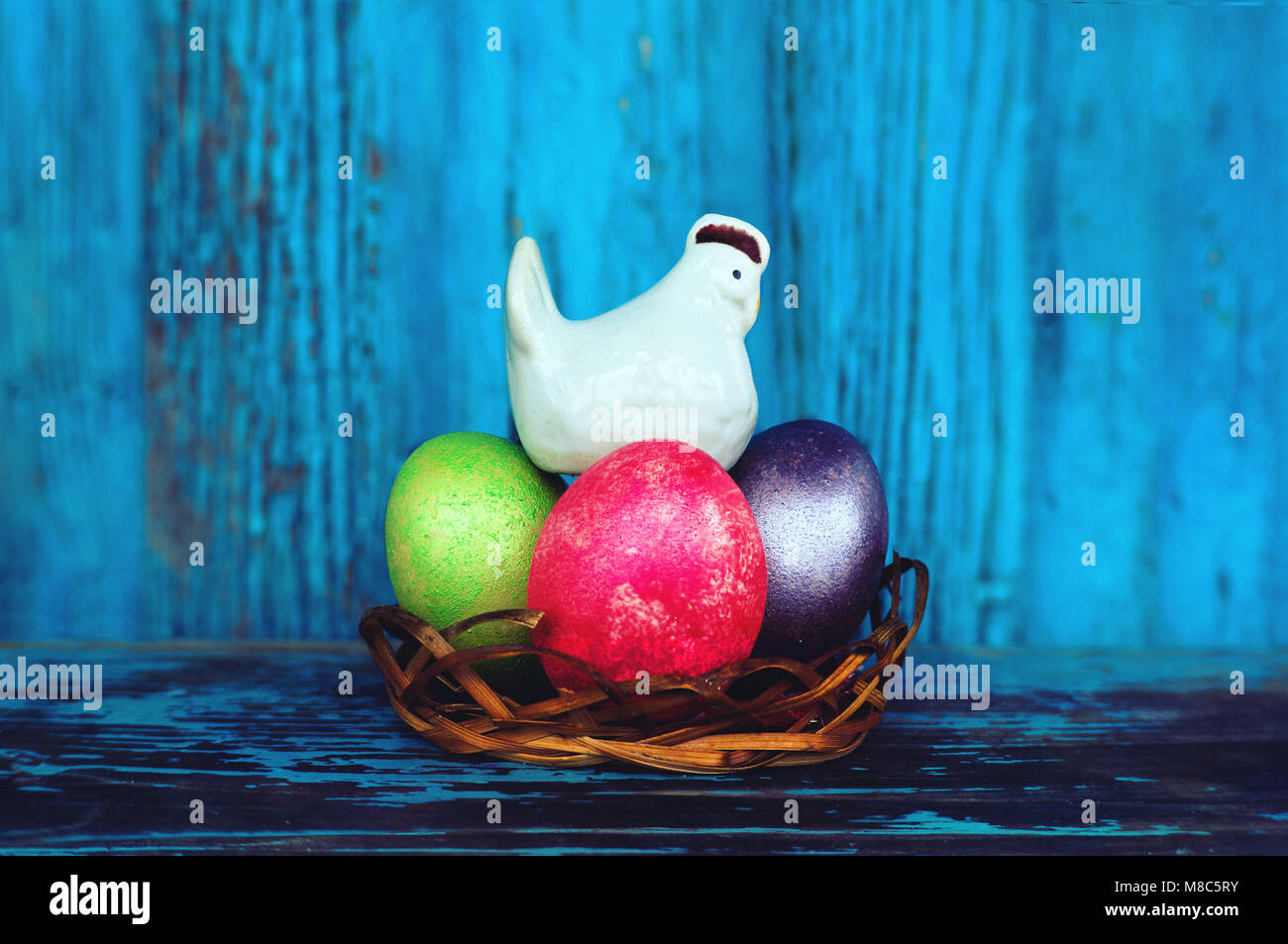 White chicken salt shaker and multicolored painted eggs on vintage wooden background. Easter's decorative ornaments. Background. chicken hen incubates Stock Photo
