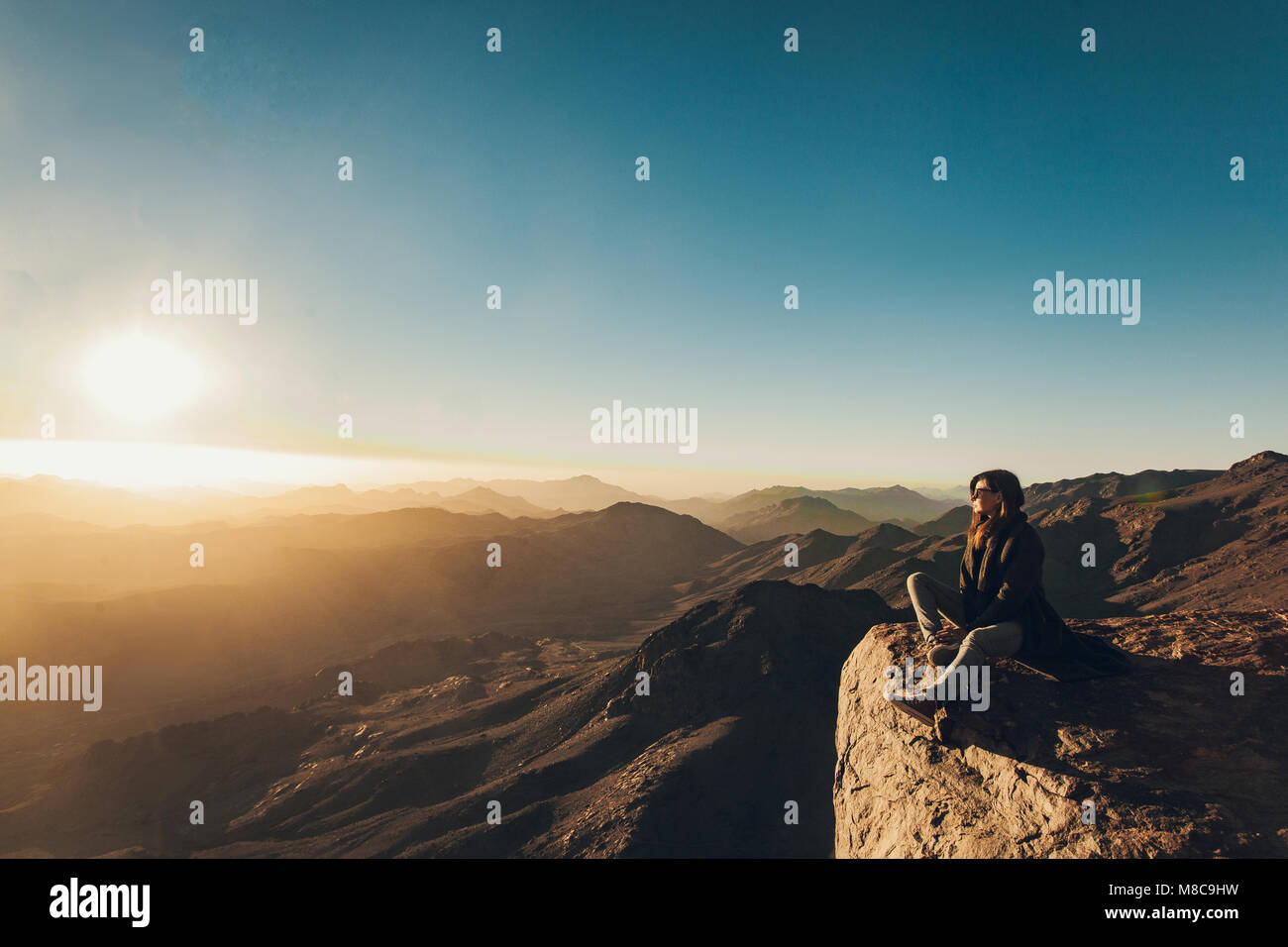 Woman sits on edge of cliff on Mount Sinai and looks at beautiful sunrise in Egypt. Stock Photo
