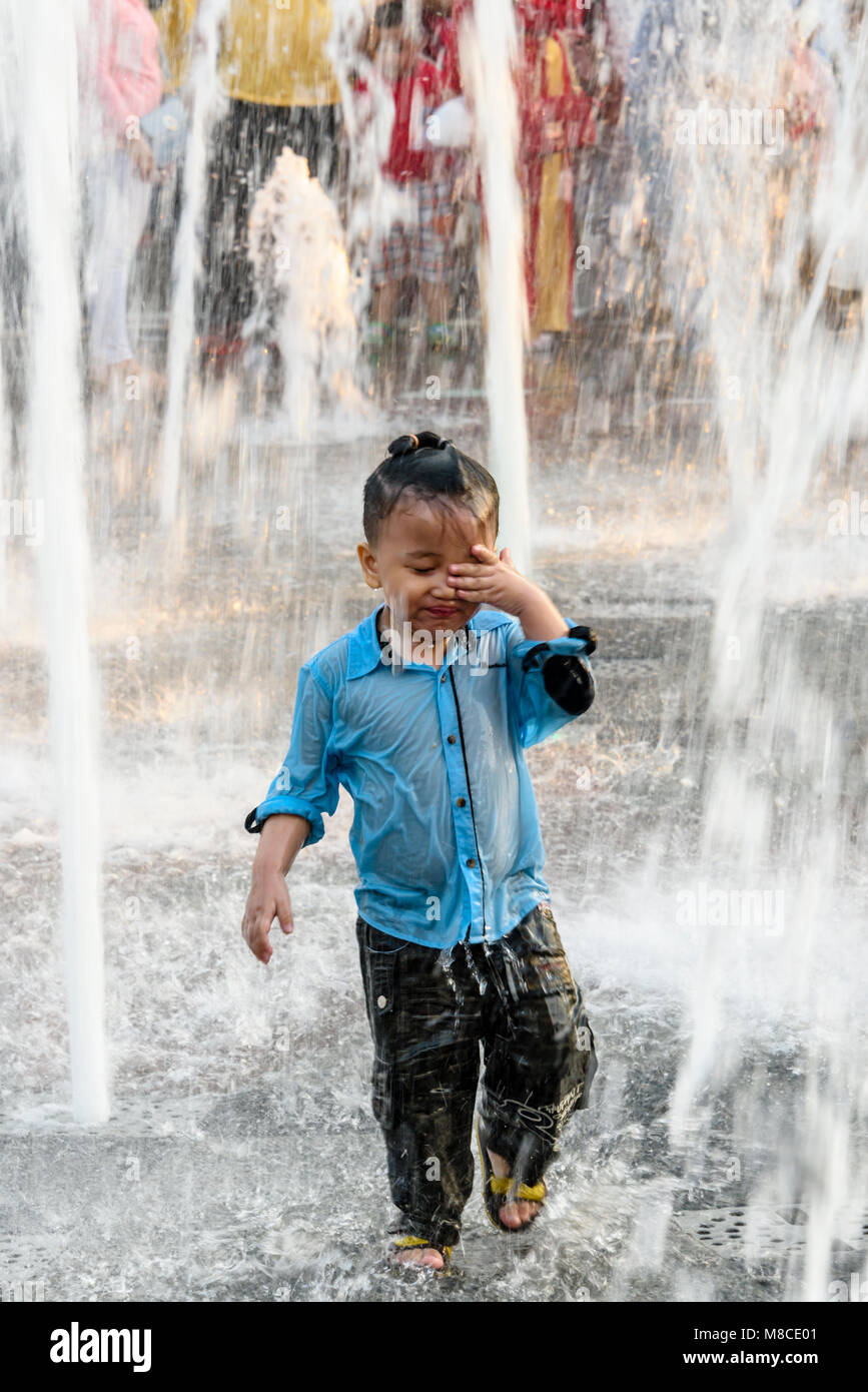 A young boy plays in the water from a street fountain, Ho Chi Minh City, Saigon, Vietnam Stock Photo