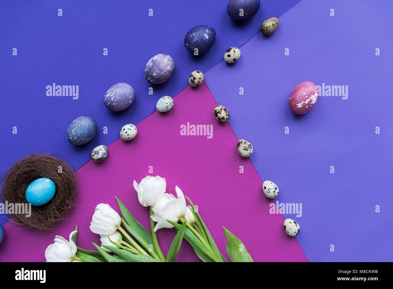flat lay with painted eggs with nest and spring flowers on background ...