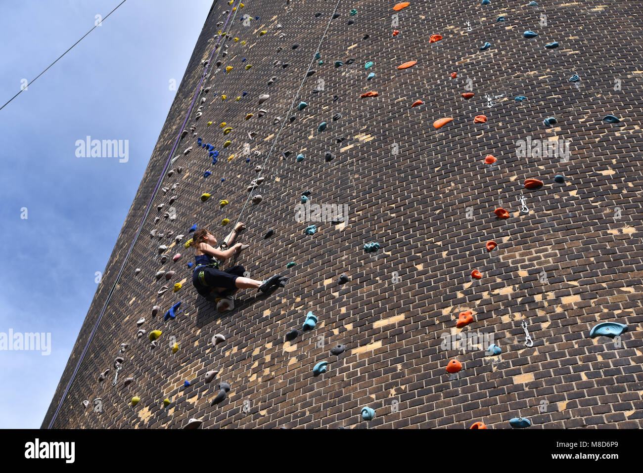 woman climbs up an artificial rock wall - secured with a rope against falling Stock Photo