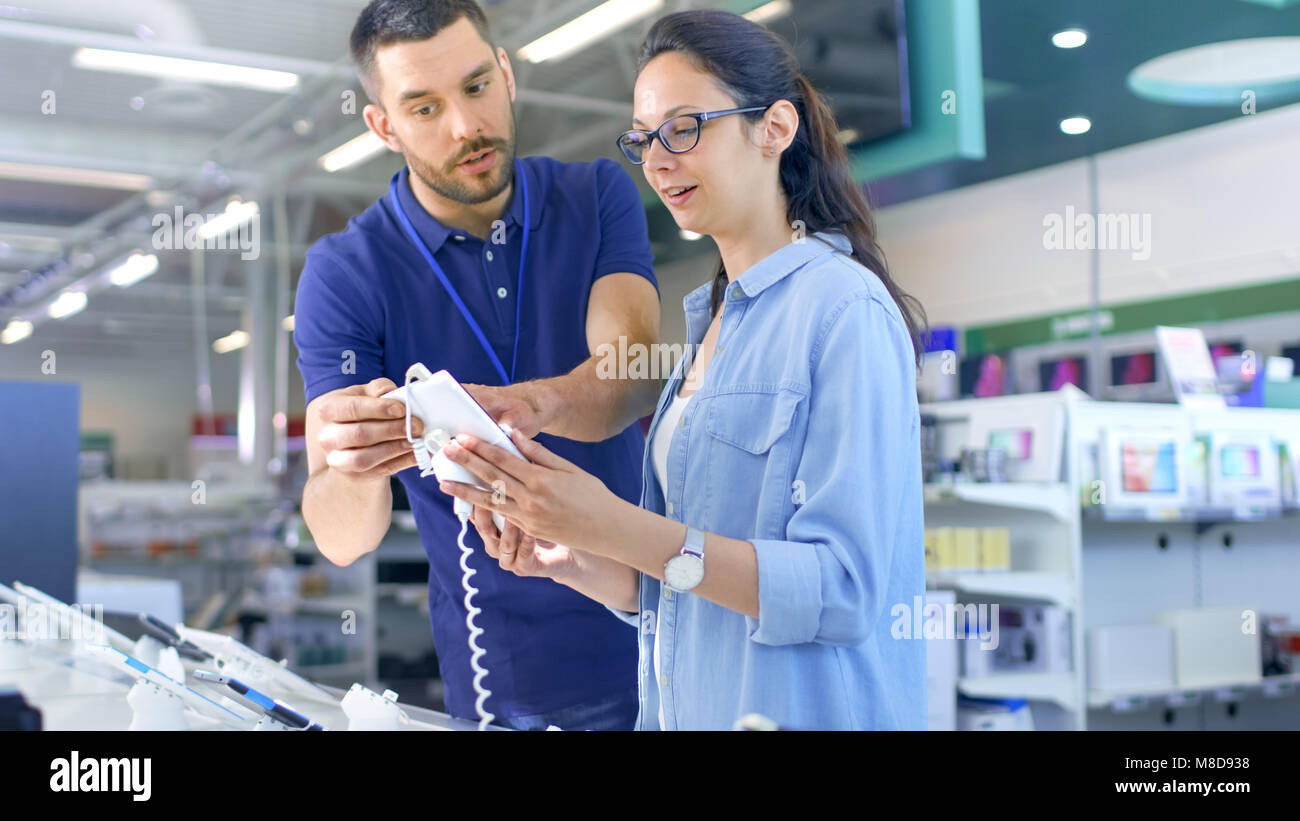 In the Electronics Store Consultant Gives Professional Advice to a Young Woman, She Considers Buying New Tablet Computer and Needs Expert Opinion. Stock Photo