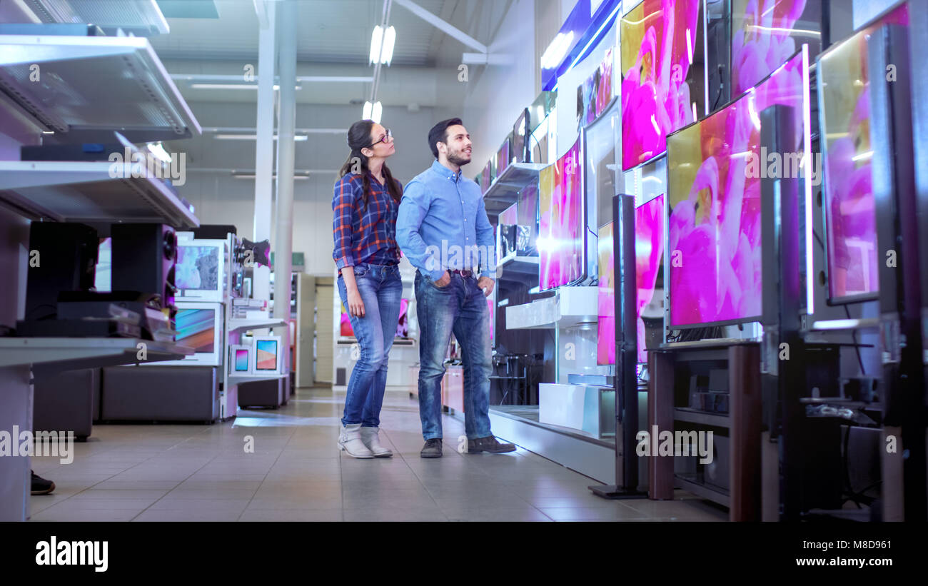 In the Electronics Store Young Couple is Choosing Which a New Model of 4K TV's is Best for Their Home and Budget. Stock Photo