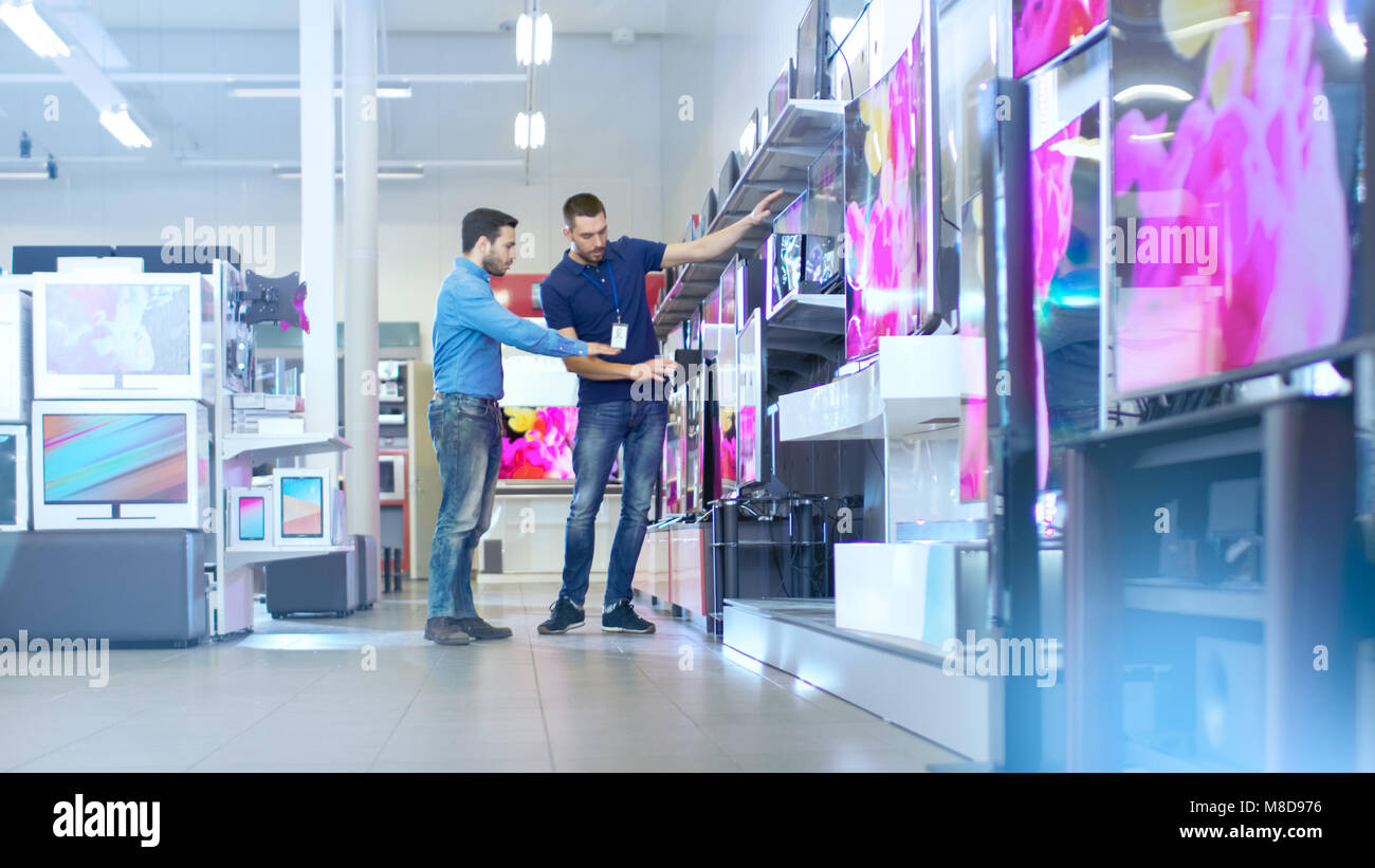 In the Electronics Store Professional Consultant Shows Latest 4K UHD TV's to a Young Man, They Talk about Specifications and What Model is Best Stock Photo